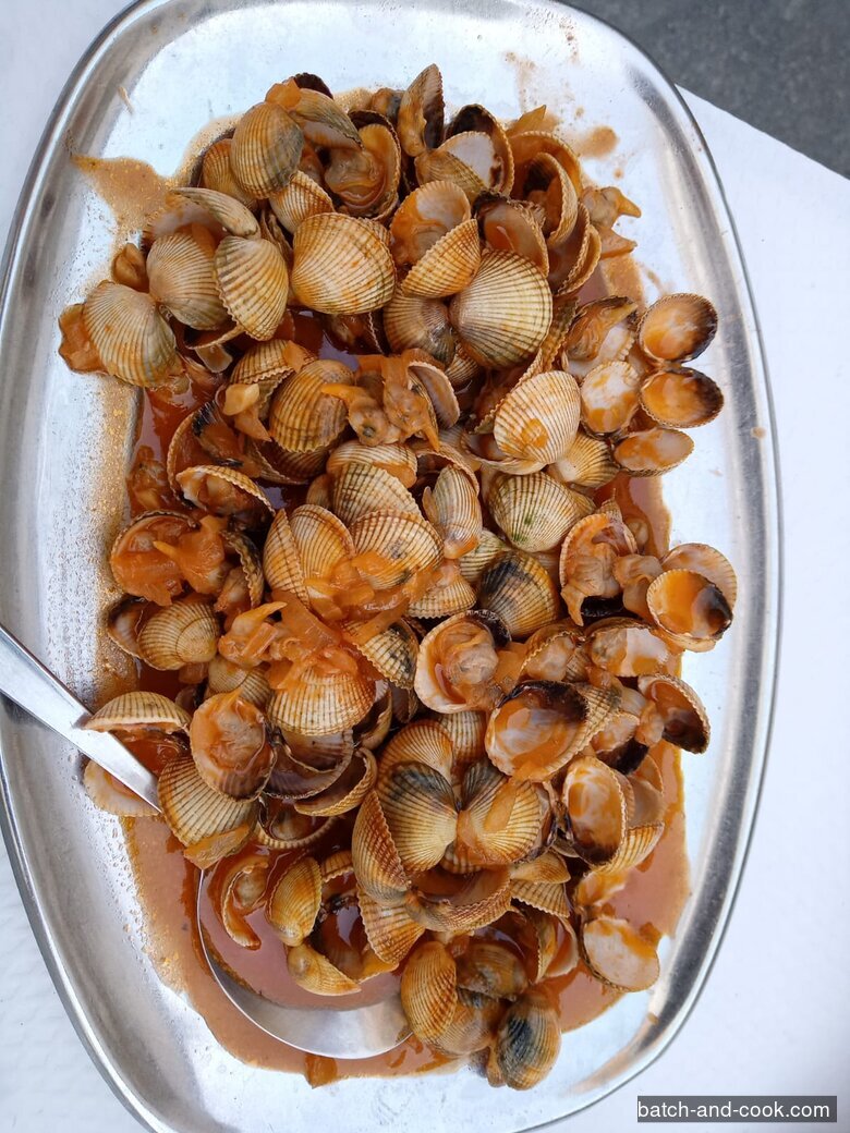 Un plat de berbigão (coques) mijotées en sauce tomate aux oignons, dans un plat ovale en inox